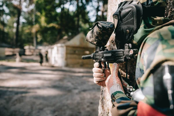 Enfoque selectivo del jugador de paintball en máscara de gafas y camuflaje con el objetivo de pistola de paintball al aire libre - foto de stock