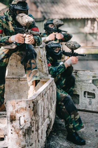 Paintball players aiming with marker guns from broken car outdoors — Stock Photo