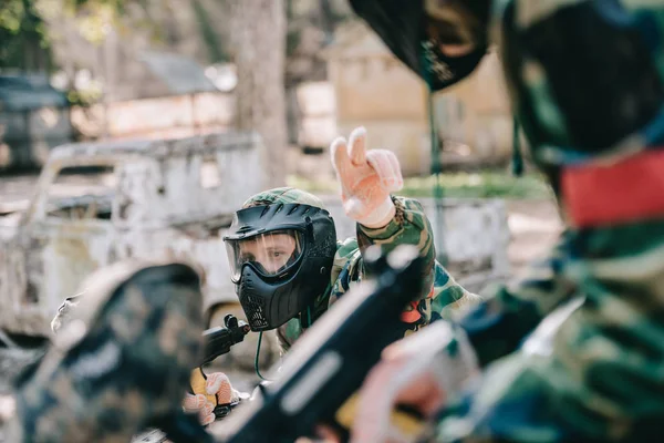 Male paintball player in camouflage with marker gun uniform pointing by fingers to his team outdoors — Stock Photo