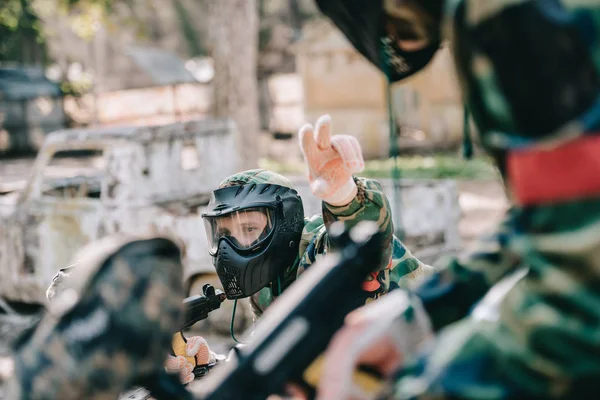 Jugador de paintball masculino en camuflaje con marcador uniforme apuntando con los dedos a su equipo al aire libre - foto de stock