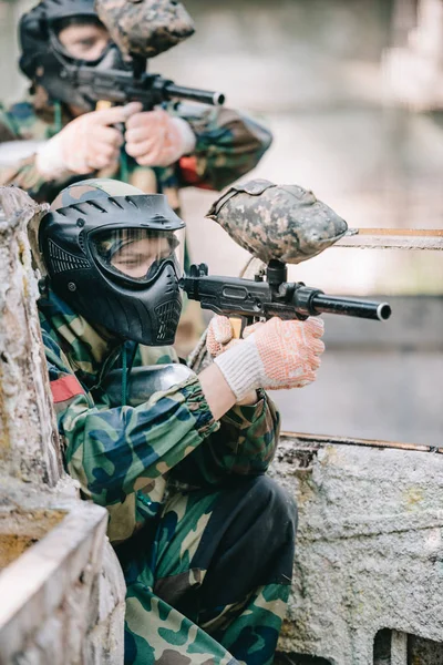 Side view of concentrated paintball player in protective mask aiming with marker gun outdoors — Stock Photo