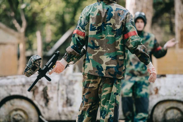 Teilansicht von Paintballspielern in Tarnuniform, die in der Nähe eines kaputten Autos im Freien ruhen — Stockfoto