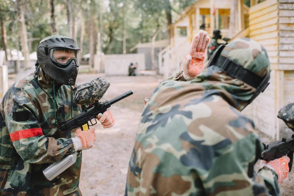 Vista trasera del jugador de paintball en uniforme de camuflaje haciendo sígueme gesto a su equipo al aire libre - foto de stock