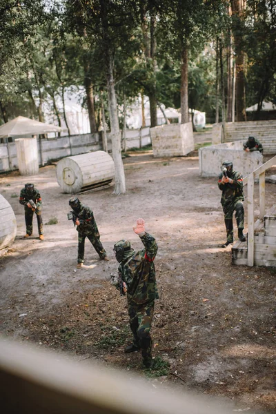 Vista de ángulo alto del jugador de paintball en uniforme haciendo sígueme gesto a su equipo con pistolas de paintball al aire libre - foto de stock