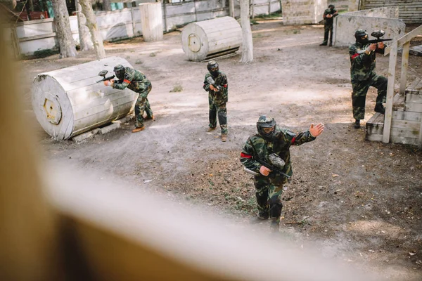 High angle view of paintball player in uniform pointing by hand to his team with markers guns outdoors — Stock Photo