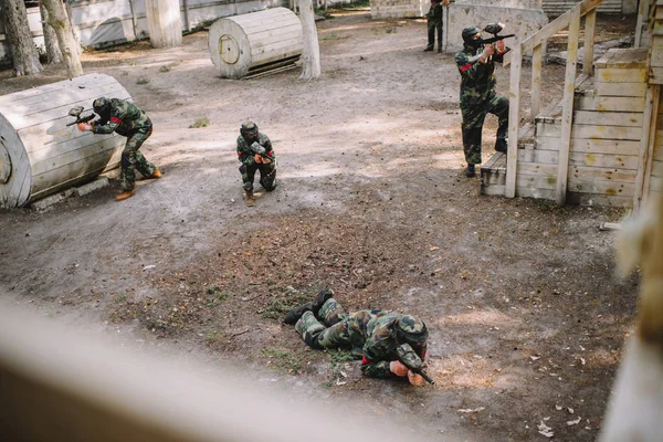 Vista de ángulo alto del equipo de paintball en uniforme y máscaras protectoras jugando paintball con marcadores armas al aire libre - foto de stock