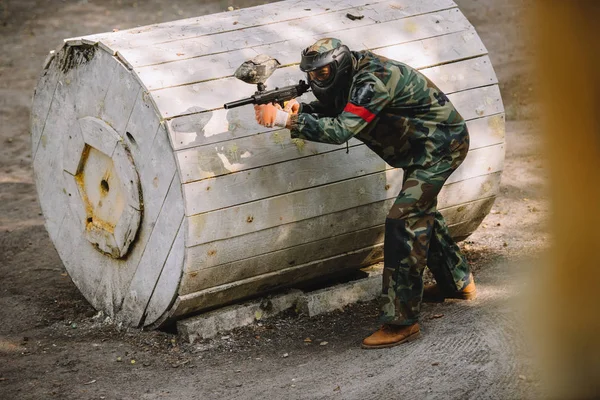 Joueur de paintball masculin en masque de masque et camouflage visant par pistolet de paintball à l'extérieur — Photo de stock