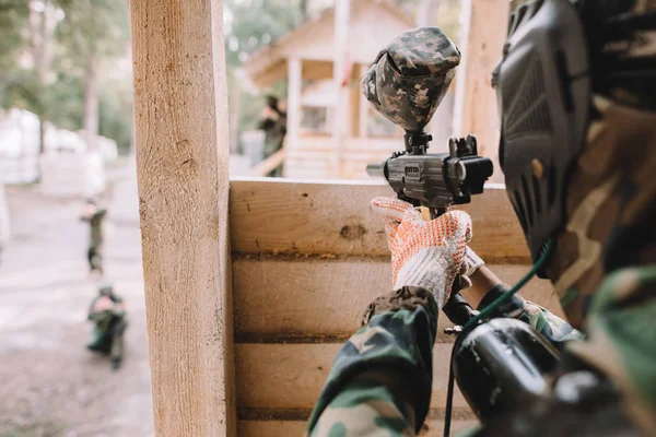 Selective focus of paintball player in camouflage uniform aiming by paintball gun from wooden tower outdoors — Stock Photo