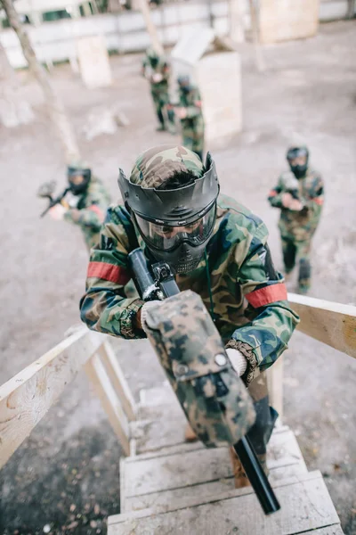 High angle view of paintball player aiming by marker gun and running on staircase while his team standing behind outdoors — Stock Photo