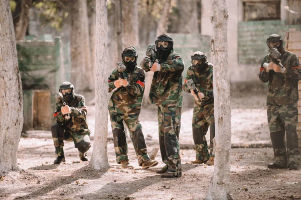 Paintball team in uniform and protective masks aiming by paintball guns outdoors — Stock Photo