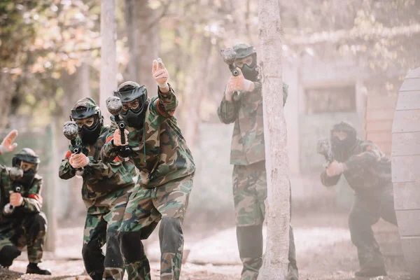 Paintball player in camouflage uniform pointing by hand to his team with markers guns outdoors — Stock Photo