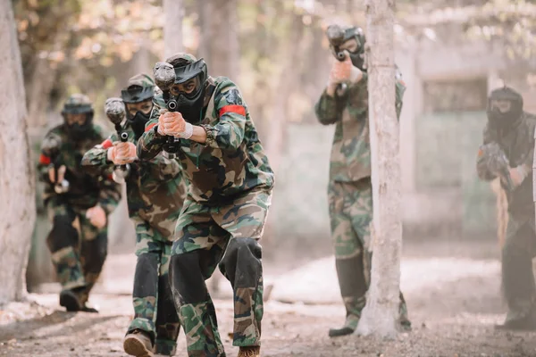 Paintball team in uniform and protective masks aiming by paintball guns outdoors — Stock Photo