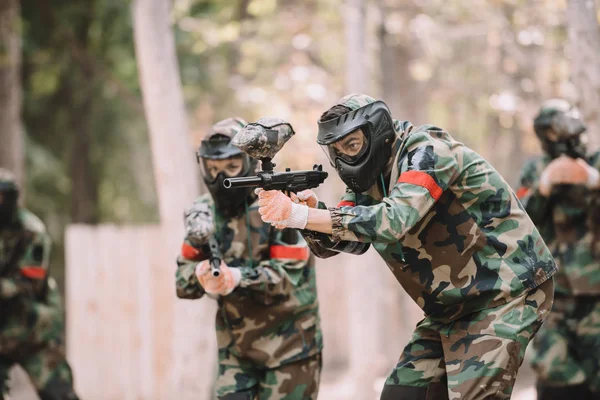 Paintball team in uniform and protective masks aiming by paintball guns outdoors — Stock Photo