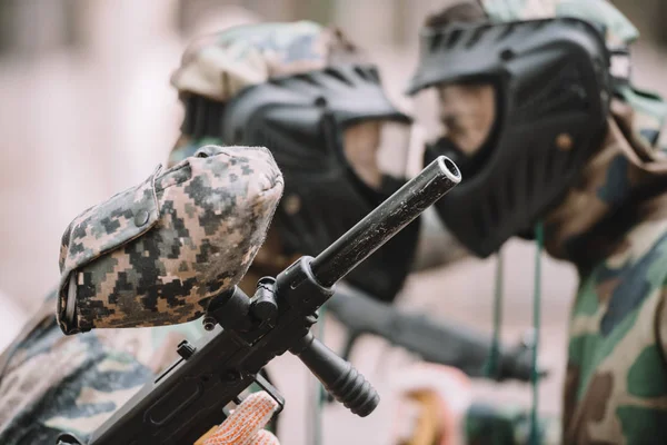 Enfoque selectivo de la pistola marcadora en la mano del jugador de paintball de pie cara a cara con otro jugador al aire libre - foto de stock