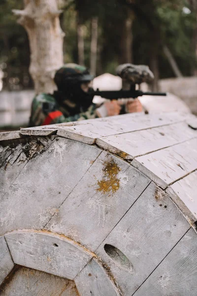 Foco seletivo de salpicos de paintball no barril de madeira e paintball jogador atirando ao ar livre — Fotografia de Stock