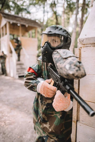 Fokussierter männlicher Paintballer in Brillenmaske, der von Paintball-Spritzern bedeckt ist, die im Freien mit Marker-Pistole zielen — Stockfoto