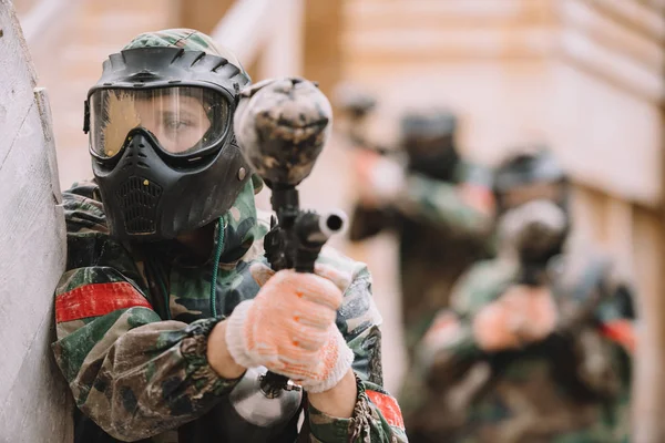 Paintballer masculino en máscara de gafas cubierto por salpicaduras de paintball con el objetivo de pistola marcador al aire libre - foto de stock