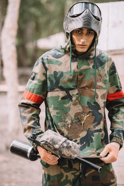 Young male paintball player in camouflage covered by paintball splash outdoors — Stock Photo