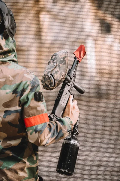 Vista parcial del jugador de paintball masculino en máscara de gafas y camuflaje sosteniendo pistola de paintball al aire libre - foto de stock