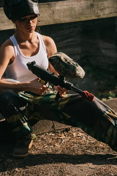 Concentrou paintballer feminino em singlet branco e máscara de óculos carregando paintball arma ao ar livre — Fotografia de Stock