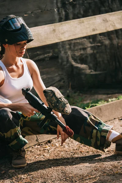 Paintballer feminino em singlet branco e máscara de óculos segurando paintball arma ao ar livre — Fotografia de Stock