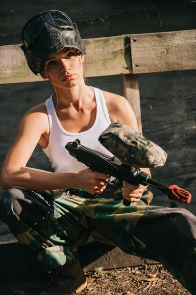 Beautiful young female paintballer in white singlet and goggle mask holding paintball gun outdoors — Stock Photo