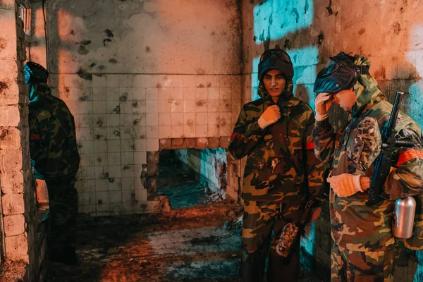 Jeunes joueurs masculins de paintball en uniforme et masques protecteurs reposant dans un bâtiment abandonné — Photo de stock