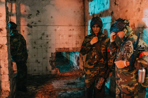 Young male paintball players in uniform and protective masks resting in abandoned building — Stock Photo