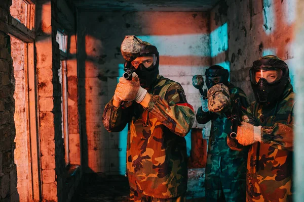 Equipo de paintball en uniforme y máscaras protectoras apuntando por pistolas de paintball en edificio abandonado - foto de stock