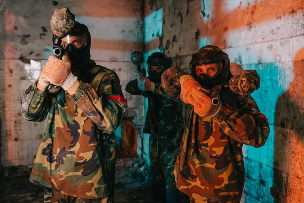 Paintball team in uniform and protective masks aiming by paintball guns in abandoned building — Stock Photo