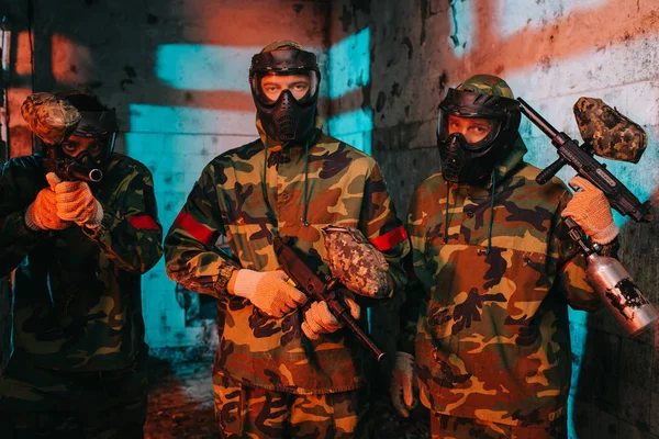 Portrait of paintball team in uniform and protective masks with paintball guns in abandoned building — Stock Photo