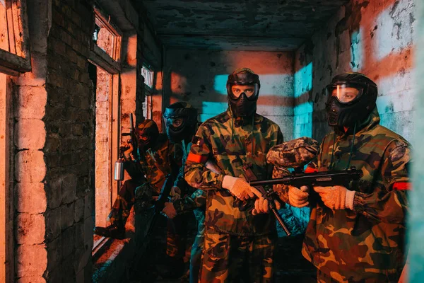 Paintball team in uniform and protective masks standing with paintball guns in abandoned building — Stock Photo