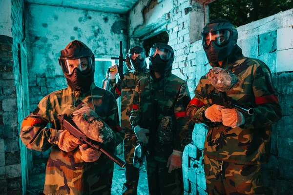 Paintball team in uniform and protective masks standing with paintball guns in abandoned building — Stock Photo