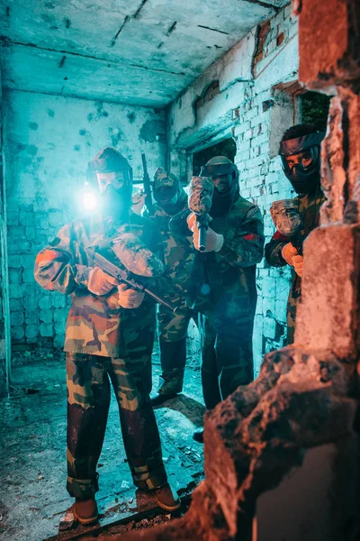 Paintball team in uniform and protective masks with paintball guns in abandoned building — Stock Photo