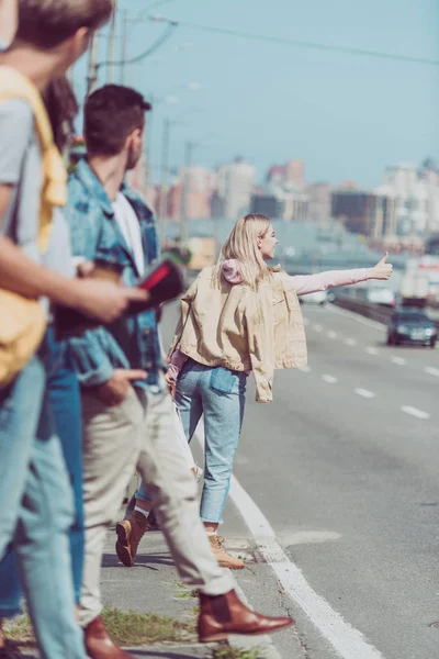 Woman hitchhiking on road while friends standing behind — Stock Photo