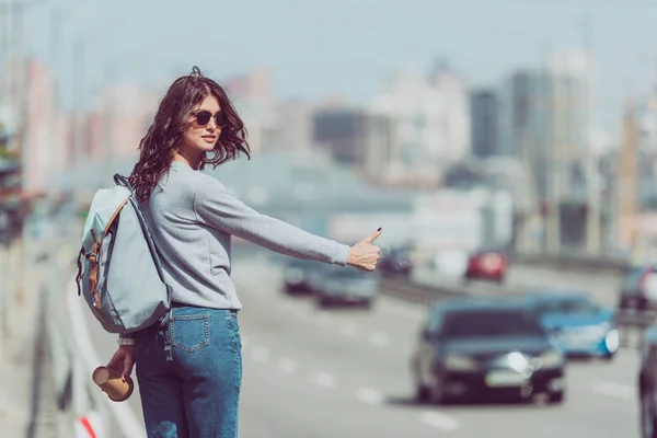 Mujer joven con mochila y café para hacer autostop en la carretera - foto de stock