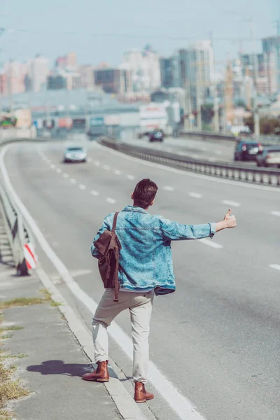 Back view of man hitchhiking alone on road — Stock Photo