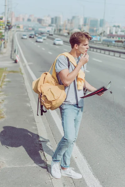 Молодой человек с картой и рюкзаком ищет пункт назначения — стоковое фото