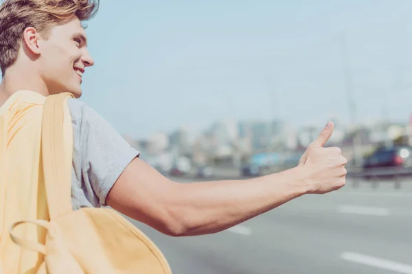 Smiling young man hitchhiking on road — Stock Photo