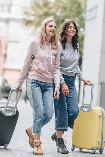 Female tourists with backpacks and baggage walking on city street — Stock Photo