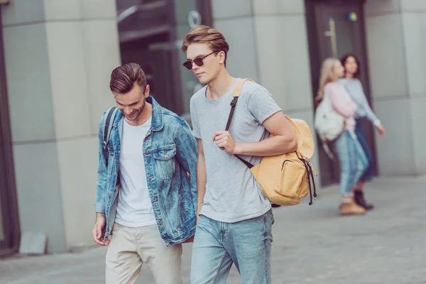 Jóvenes viajeros con mochilas caminando por la calle de la ciudad - foto de stock