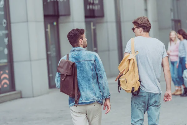 Rear view of travelers with backpacks walking on city street — Stock Photo