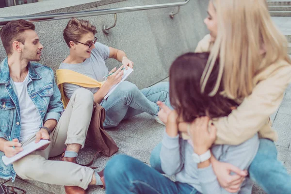 Turistas jóvenes descansando en los escalones en la calle de la nueva ciudad - foto de stock