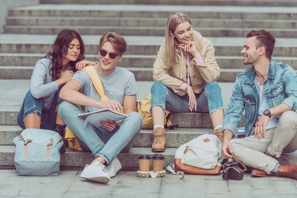 Young tourists resting on steps on street of new city — Stock Photo