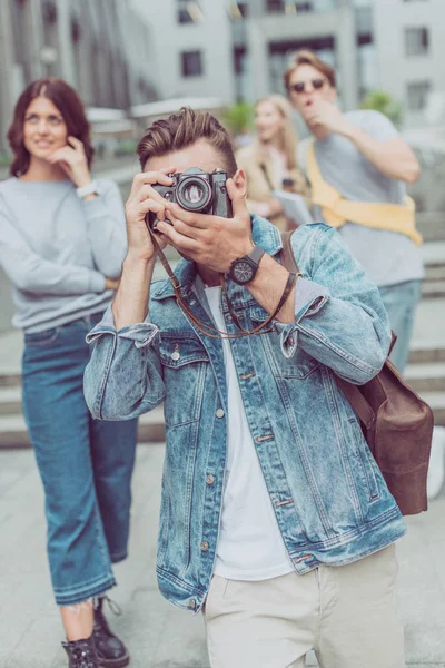 Selective focus of tourist taking picture on photo camera with friends behind on street — Stock Photo