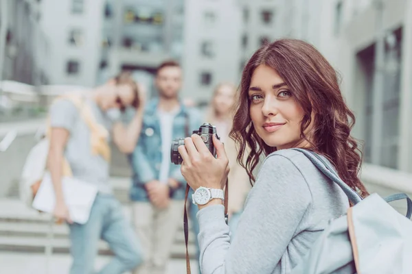 Atractiva chica morena con cámara de fotos caminando en la ciudad con amigos - foto de stock