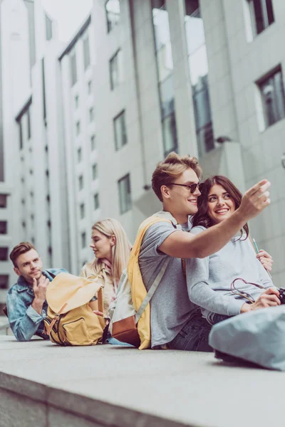 Giovani belle coppie sedute in città, mentre l'uomo sorridente mostra qualcosa — Foto stock