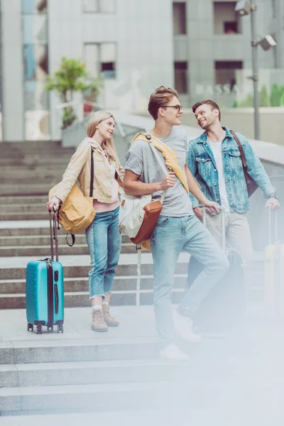 Young friends with backpacks and travel bags on stairs in city — Stock Photo