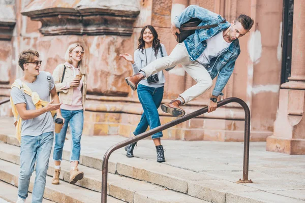 Jóvenes amigos elegantes caminando en la ciudad mientras el hombre salta sobre la barandilla - foto de stock