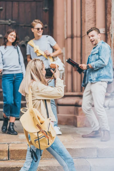 Girl taking photo of funny friends on camera in city — Stock Photo